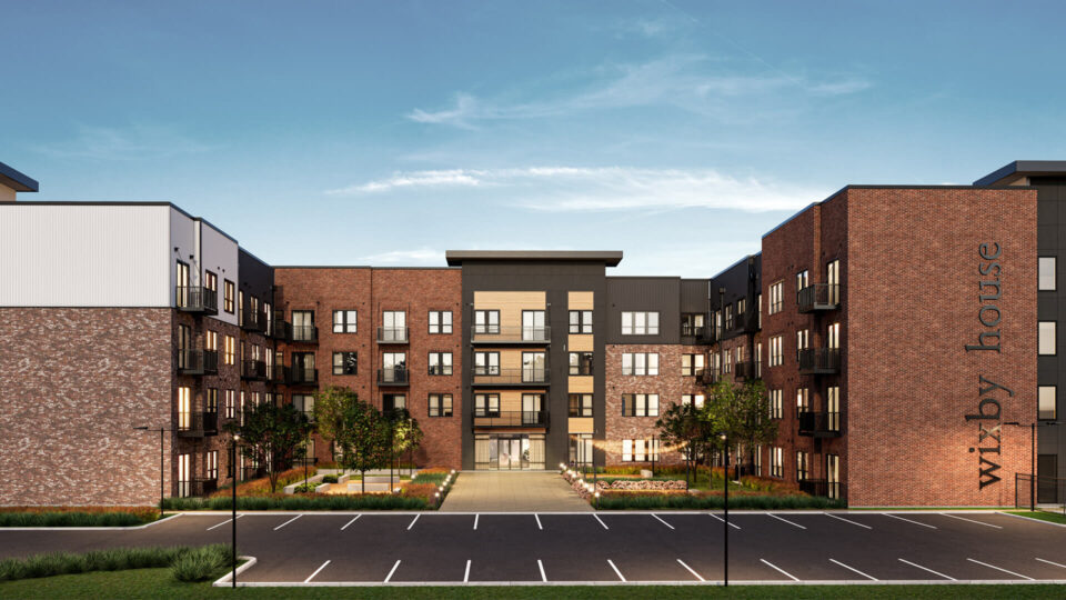 Rendering of a multi-story brick apartment building labeled 'Wixby House' with black accents and a landscaped entrance under a clear sky. The design is modern with a mix of industrial and contemporary architectural elements.